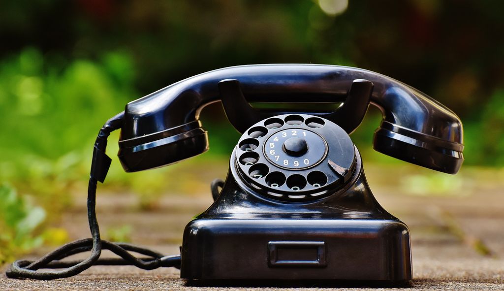 Close-up of a classic black rotary phone outdoors with a blurred green background for contact and support.